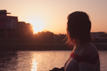 Silhouette of a girl looking at the river and sunset