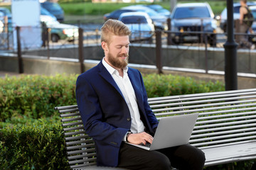 Wall Mural - Handsome young man with laptop on bench, outdoors