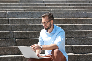 Wall Mural - Handsome man with laptop sitting on stairs outdoors