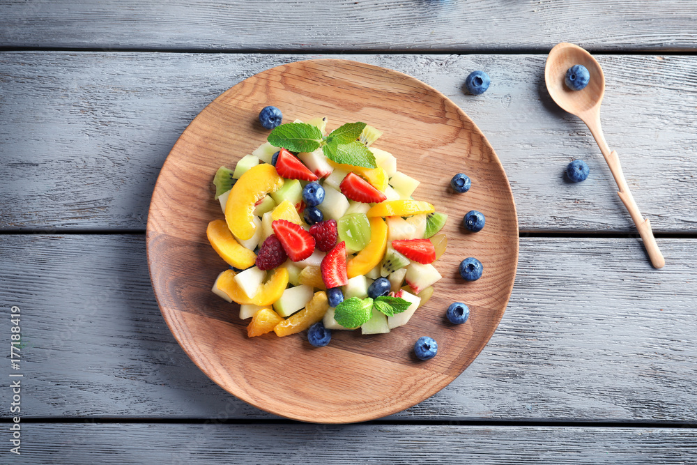 Plate with delicious fruit salad on wooden background
