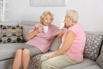 Wall Mural - Elderly women drinking coffee while sitting on sofa at home