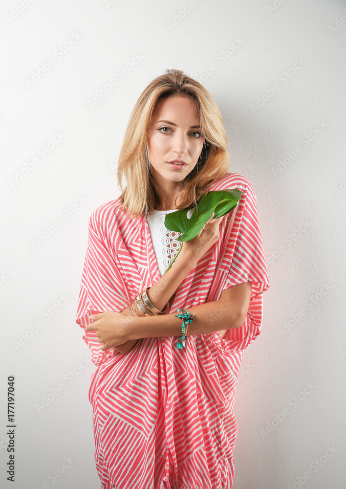 Beautiful young woman posing with tropical leaf on light background