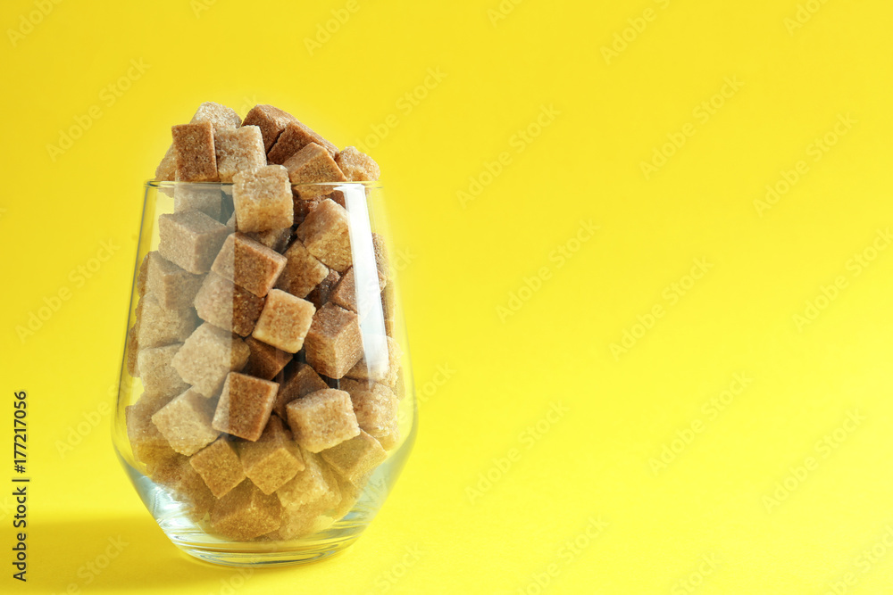 Glass full of brown sugar cubes on color background