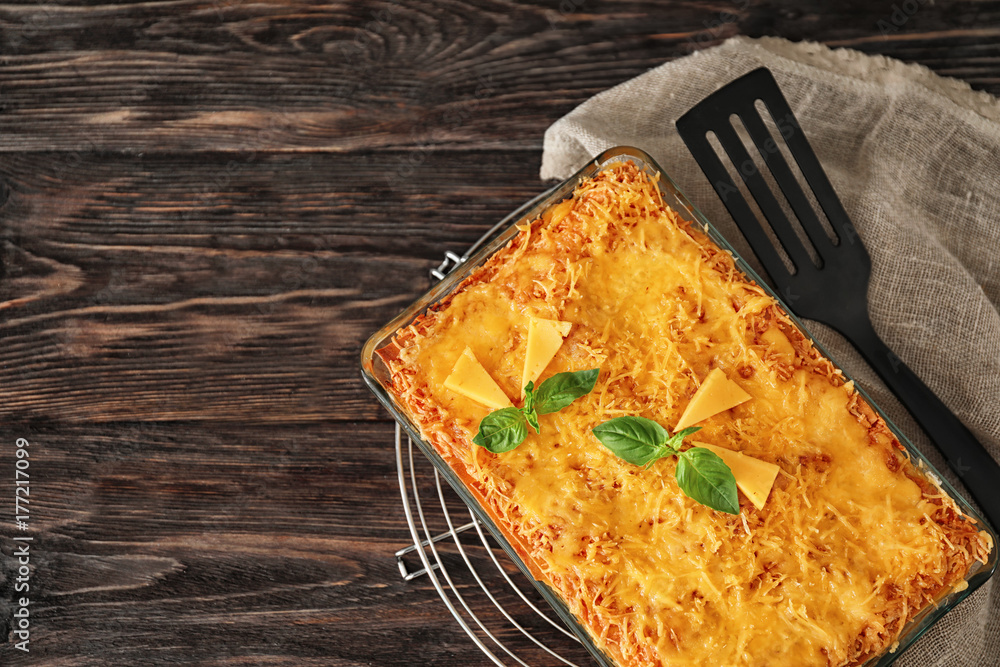 Traditional meat lasagna in baking dish on wooden table