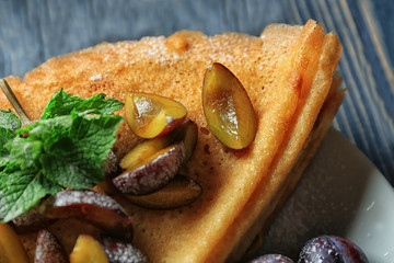 Canvas Print - Plate with tasty thin pancakes and plums on table, closeup