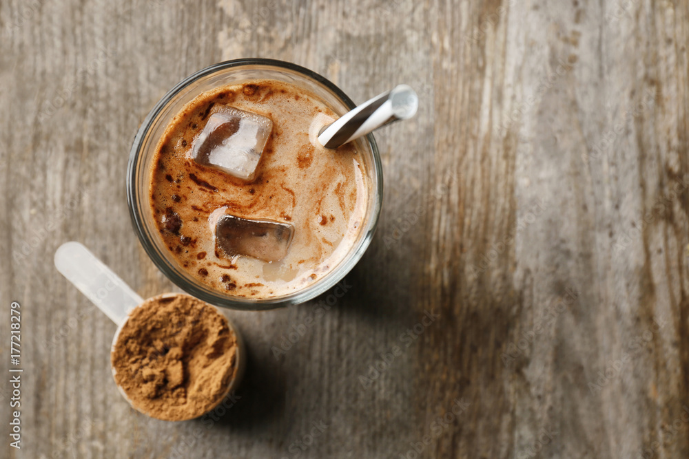 Glass with protein shake and powder in scoop on wooden table
