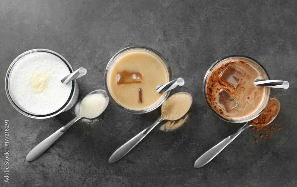 Glasses with different protein shakes and powders in spoons on table