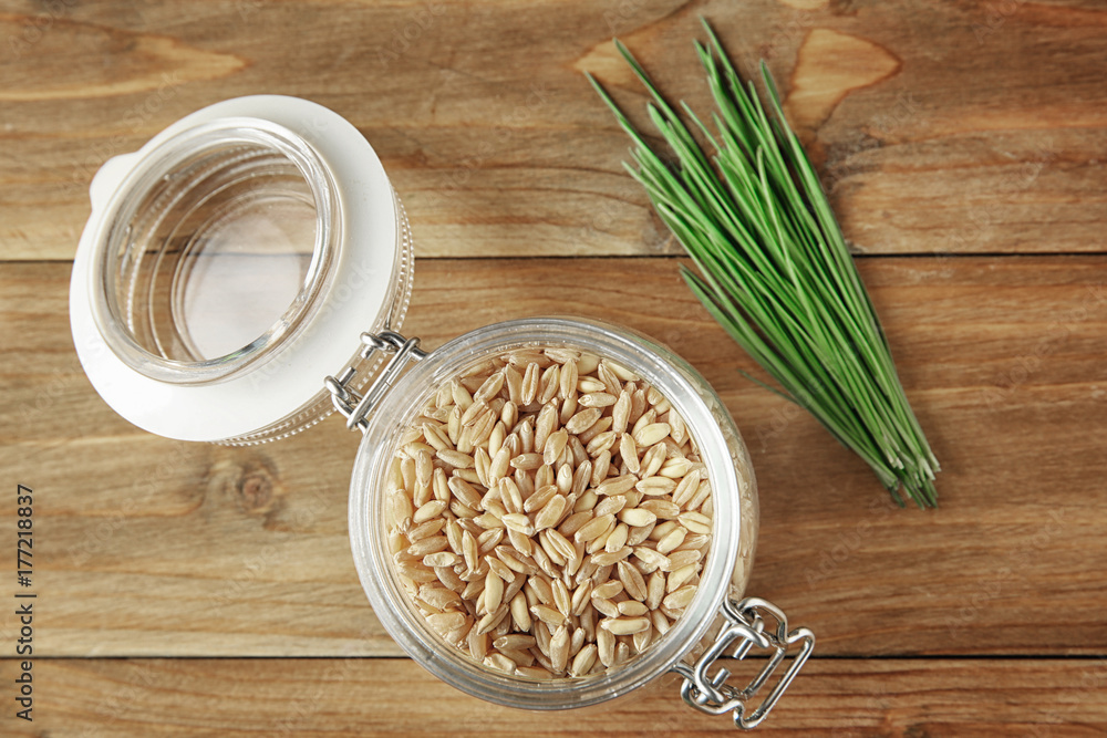 Jar of wheat grass seeds and sprouts on wooden table