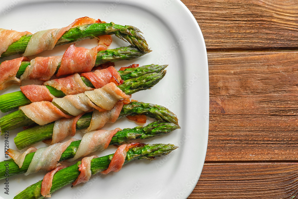 Plate with bacon wrapped asparagus on light background