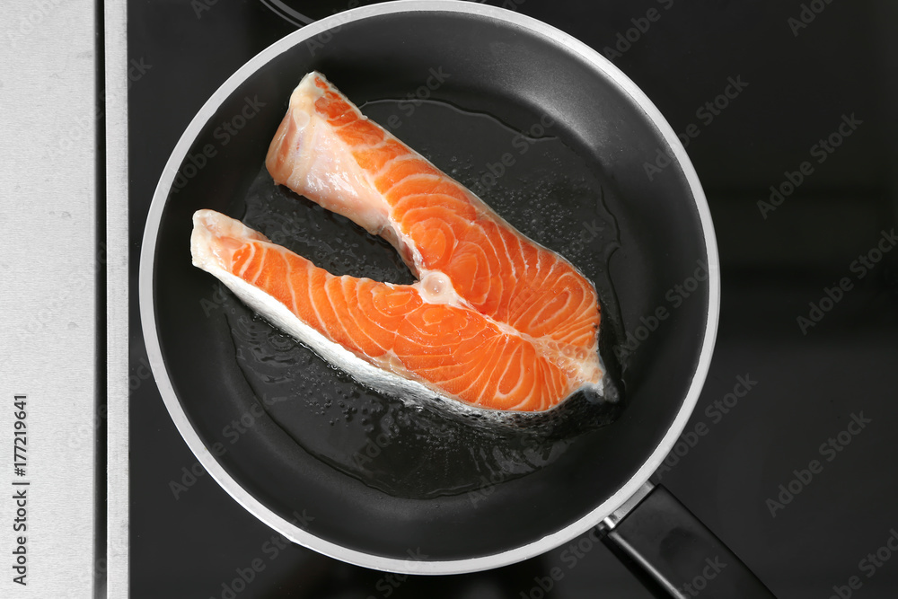 Frying pan with raw salmon steak on stove in kitchen