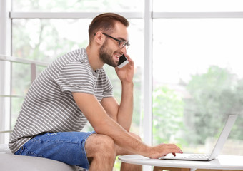 Wall Mural - Attractive young man with smartphone using laptop at home