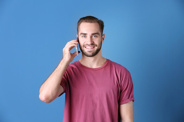 Wall Mural - Attractive young man with smartphone on color background