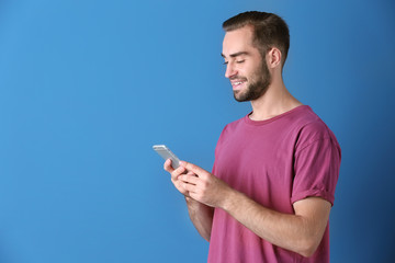 Attractive young man with smartphone on color background