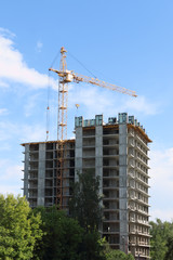 Tall crane works near tall residential building on construction site at summer day