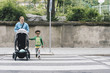 © Maskot - Mother pushing baby stroller while crossing road with son at city