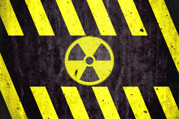 Radioactive (ionizing radiation) danger symbol with yellow and black stripes painted on a massive concrete wall with rustic texture background.