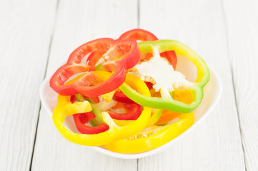 Heap of colored red and green and yellow fresh ripe raw pepper in ceramic bowl on old rural white wooden planks