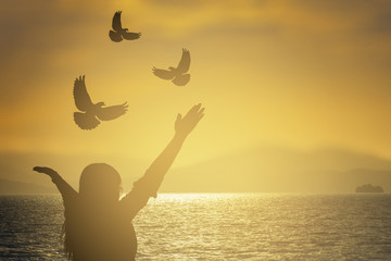 silhouette young women were  praying and free bird fly over blurred nature sunset background. hope and people concept and international day of peace.