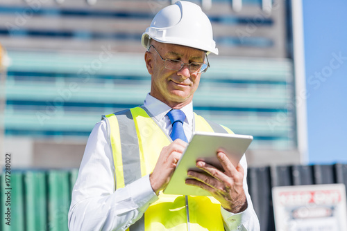 Plakat Kierownik budowy kontrolowanie strony budynku i tabletu w jego ręce