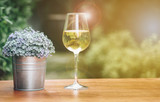 Fototapeta Lawenda - A glass of champagne and a small vase on a wooden table with a garden as the background blurred.