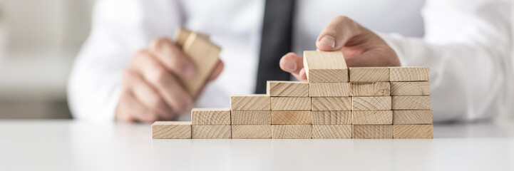 Wall Mural - Closeup of businessman arranging wooden pegs into a staircase