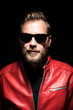 © _robbie_ - Cool man in a red leather jacket with sunglasses standing against a black background.