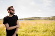 © _robbie_ - Handsome man wearing a black tshirt and jeans with dark sunglasses, standing alone on an empty field on a sunny summer day.