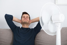 Man Sitting On Couch Cooling Off With Fan