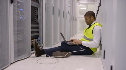 Portrait smiling engineer sitting on floor with laptop in a data center.