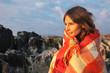 © BONNINSTUDIO/Stocksy - Young woman wrapped with plaid blanket on beautiful landscape.