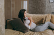 © ViDi Studio - Beautiful young woman at home lying on the sofa, relaxing in her living room and working with laptop