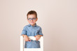 © Lea Csontos/Stocksy - Portrait of an adorable boy smiling, against a beige background kneeling on a white chair.
