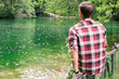 © Jovo Jovanovic/Stocksy - The back of a man sitting on a fence looking out onto a green lake in a park