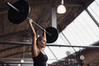 Fit woman lifting barbells over her head in a gym