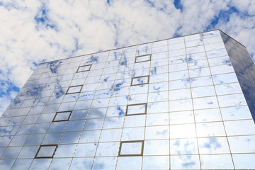 Blue clouds and sun are reflected in the glasses of windows of a modern building. Right view