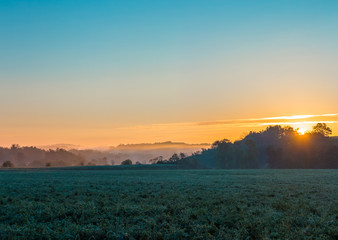 Colorful Sunrise with Misty Field and Hills in Background