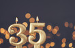 Gold number 35 celebration candle against blurred light background