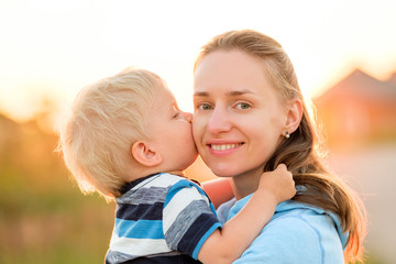 Wall Mural - Woman and child outdoors at sunset. Boy kissing his mom.