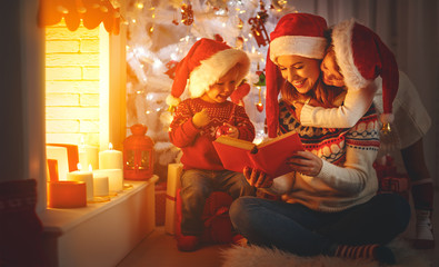 Wall Mural - family mother and children read a book at christmas near fireplace at home