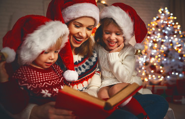 Wall Mural - family mother and children read a book at christmas near fireplace at home.