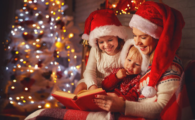 Wall Mural - family mother and children read a book at christmas near fireplace at home.