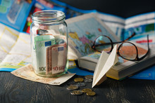 Jar With Money For A Travel, Airplane, Maps, Passport, And Other Stuff For Adventure