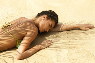 Woman is lying on the beach under palm leaf