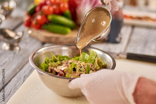 Zdjęcie XXL Szef kuchni wylewa sos na mieszaną sałatkę. Zielona zdrowa sałatka w nierdzewnym pucharze w restauraci. Szef kuchni gotowania danie w kuchni restauracji.