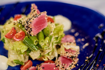 Wall Mural - Close up of delicious fresh salad. Salad nisuaz wih lettuce, asparagus, cherry tomatoes, sesame on plate. Delicious restaurant cuisine.