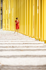 Woman in red dress on the modern yellow building wall background. General plan with abstract geometric composition