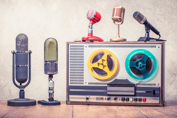 Wall Mural - Retro reel to reel tape recorder from 60s and studio microphones on wooden table front concrete wall background. Vintage style filtered photo