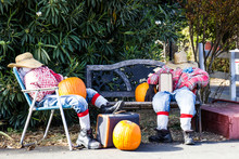 Two Halloween Scarecros Sitting With Suitcases