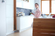 © lenets_tan - Woman using mobile phone standing in modern kitchen.