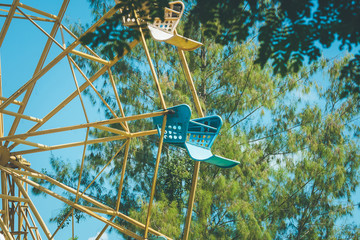 Vintage retro image close up part of colorful ferris wheel with green tree and blue sky background.